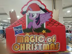 Size: 1920x1440 | Tagged: safe, artist:starlessnight22, derpibooru import, official, twilight sparkle, twilight sparkle (alicorn), alicorn, pony, candy, candy cane, christmas, cute, female, food, hasbro, hasbro logo, hat, irl, magic of christmas, mare, nose wrinkle, photo, raised hoof, retail, santa hat, scrunchy face, sitting, spread wings, standee, store display, wide eyes