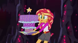 Size: 1100x618 | Tagged: safe, derpibooru import, screencap, sunset shimmer, equestria girls, legend of everfree, book, cake, camp everfree outfits, clothes, crystal gala, food, legend you were meant to be, shorts, solo