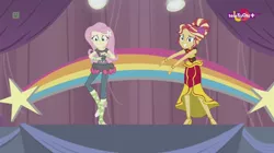 Size: 1136x638 | Tagged: safe, derpibooru import, screencap, fluttershy, sunset shimmer, dance magic, equestria girls, spoiler:eqg specials, alternate hairstyle, awkward smile, ballet slippers, canterlot high, clothes, dress, duo, female, high heels, rainbow, shoes, skirt, stars, teletoon, tutu