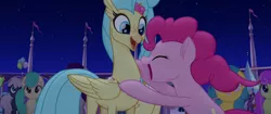 Size: 1920x804 | Tagged: safe, derpibooru import, screencap, bell perin, pinkie pie, princess skystar, unnamed pony, classical hippogriff, earth pony, hippogriff, pony, my little pony: the movie, background pony, crowd, duo focus, female, happy, hug, incoming hug, jewelry, mare, necklace, rainbow (song), seashell, seashell necklace, smiling