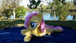 Size: 3264x1836 | Tagged: safe, artist:joltage, derpibooru import, fluttershy, pegasus, pony, blanket, crossed legs, female, irl, lake, lying down, outdoors, photo, plushie, solo