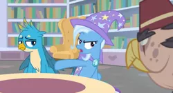 Size: 1600x862 | Tagged: safe, derpibooru import, screencap, gallus, grampa gruff, trixie, gryphon, pony, unicorn, a horse shoe-in, blind eye, book, cape, chair, clothes, female, fez, hat, library, male, mare, pouting, sad, table, trio, trixie's cape, trixie's hat, unamused, upset