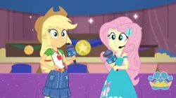 Size: 1057x594 | Tagged: safe, derpibooru import, screencap, applejack, fluttershy, best in show: the victory lap, equestria girls, equestria girls series, spoiler:eqg series (season 2), looking at you, microphone, smiling