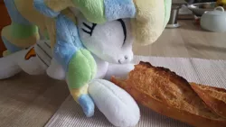 Size: 1207x679 | Tagged: safe, artist:ketika, derpibooru import, vapor trail, pegasus, pony, baguette, bread, cute, eating, eyes closed, food, happy, irl, kitchen, lying down, photo, plushie, solo, table, vaporbetes