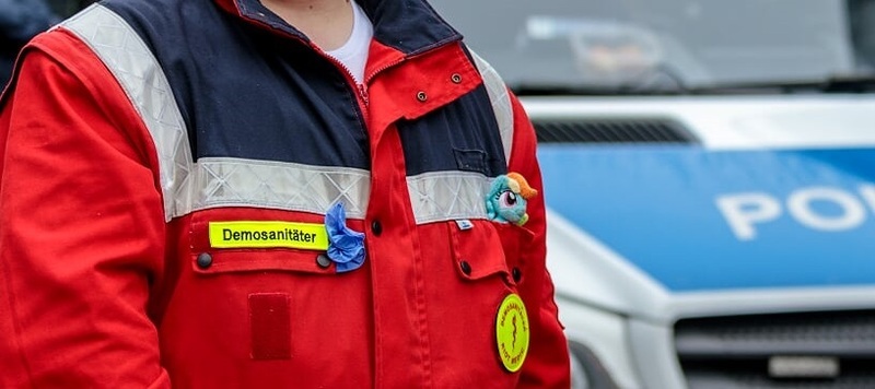 Size: 817x364 | Tagged: safe, artist:doc rainbow, derpibooru import, rainbow dash, human, demo, demonstration, emt, germany, irl, irl human, medic, on duty, paramedic, photo, plushie, police car, riot, riotmedic
