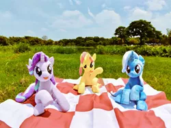 Size: 1024x768 | Tagged: safe, artist:nekokevin, derpibooru import, starlight glimmer, sunset shimmer, trixie, pony, unicorn, series:nekokevin's glimmy, female, irl, looking at you, magical trio, mare, open mouth, photo, picnic blanket, plushie, raised hoof, sitting, smiling, tree, underhoof