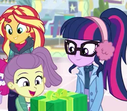 Size: 755x658 | Tagged: safe, derpibooru import, screencap, lily pad (equestria girls), little red, sci-twi, sunset shimmer, twilight sparkle, equestria girls, equestria girls series, holidays unwrapped, spoiler:eqg series (season 2), canterlot mall, clothes, coat, cropped, cute, earmuffs, female, gift giving, happy, offscreen character, ponytail, smiling, winter outfit