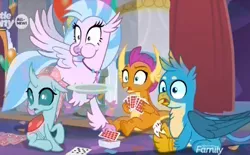 Size: 1024x634 | Tagged: safe, derpibooru import, screencap, gallus, ocellus, silverstream, smolder, changedling, changeling, classical hippogriff, dragon, gryphon, hippogriff, she's all yak, card game, dragoness, eating, female, flying, jewelry, male, necklace, needs more jpeg, plate, playing card, puffy cheeks