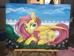 Size: 900x675 | Tagged: safe, artist:dvixie, banned from derpibooru, deleted from derpibooru, derpibooru import, fluttershy, pegasus, pony, canvas, cute, female, fence, flower, flower in hair, grass, lying down, mare, open mouth, painting, prone, shyabetes, signature, solo, traditional art