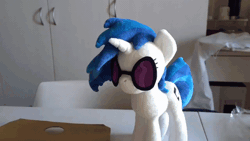 Size: 800x450 | Tagged: safe, artist:nekokevin, derpibooru import, vinyl scratch, human, pony, unicorn, absurd file size, absurd gif size, animated, chair, female, gif, glasses, grabbing, hand, irl, irl human, magnet, magnetic, mare, offscreen character, photo, plushie, smiling, solo focus, sunglasses, table, wrong eye color