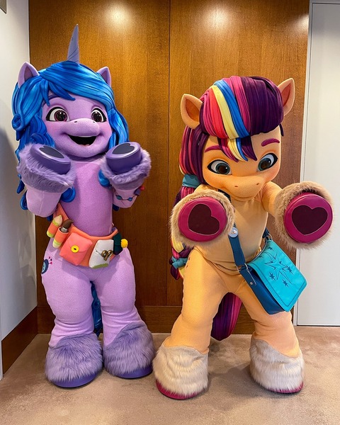 Size: 1080x1350 | Tagged: safe, derpibooru import, official, izzy moonbow, sunny starscout, anthro, earth pony, human, pony, unicorn, 2022, bag, belt, cutie mark, fursuit, g5, image, irl, irl human, jpeg, mascot, mascot costume, outstretched arms, photo, ponysuit, raised hoof, smiling, wide eyes, wide hips