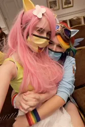 Size: 1377x2048 | Tagged: safe, artist:darknightprincess, artist:magicalmysticva, derpibooru import, fluttershy, rainbow dash, human, clothes, convention, cosplay, costume, couple, cute, face mask, female, females only, flutterdash, goggles, holding hands, image, irl, irl human, jpeg, lesbian, mask, photo, ponyville ciderfest, shipping, sitting on lap