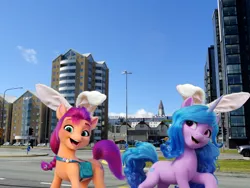 Size: 1920x1440 | Tagged: safe, artist:a-new-generation-in-real-life fan, izzy moonbow, sunny starscout, earth pony, pony, unicorn, my little pony: a new generation, bag, bunny ears, duo, easter, easter egg, female, g5, holiday, horn, iceland, image, irl, long description, looking at you, mare, open mouth, open smile, photo, png, ponies in real life, saddle bag, smiling