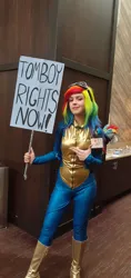 Size: 1956x4128 | Tagged: safe, derpibooru import, rainbow dash, human, bodysuit, boots, clothes, cosplay, costume, form fitting, goggles, goggles on head, image, irl, irl human, photo, plushie, png, pointing, shoes, sign, solo, tomboy, uniform, wig, wonderbolts uniform