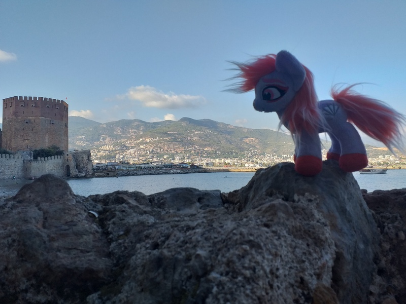 Size: 4128x3096 | Tagged: safe, artist:ferracraft, derpibooru import, sugar moonlight, earth pony, pony, alanya, city, female, g5, image, irl, jpeg, mare, ocean, photo, plushie, ponies around the world, rock, solo, standing, tower, turkey (country), water