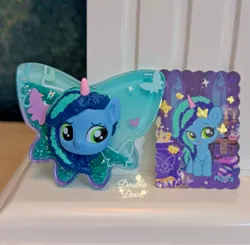 Size: 2841x2785 | Tagged: safe, derpibooru import, official, butterfly, insect, pony, g5, acrylic plastic, book, card, chibi, cutie mark, dinosaw, front view, image, irl, jpeg, merchandise, misty brightdawn, opaline's dark castle, photo, shaker, window