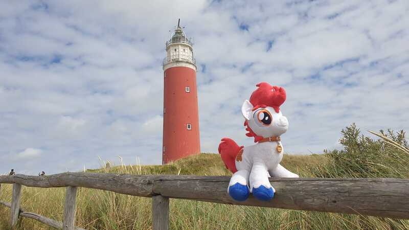 Size: 2016x1134 | Tagged: safe, derpibooru import, oc, oc:stroopwafeltje, unofficial characters only, pony, collar, fence, image, irl, jpeg, lighthouse, netherlands, photo, plushie, ponycon holland, solo, texel