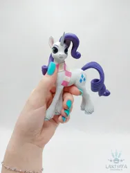 Size: 1620x2160 | Tagged: safe, alternate angle, alternate version, artist:lakterra, derpibooru import, rarity, human, pony, unicorn, clothes, craft, female, figurine, g4, hand, holding a pony, horn, image, irl, jpeg, mare, photo, polymer clay, scarf, signature, simple background, striped scarf, tail, unshorn fetlocks, white background