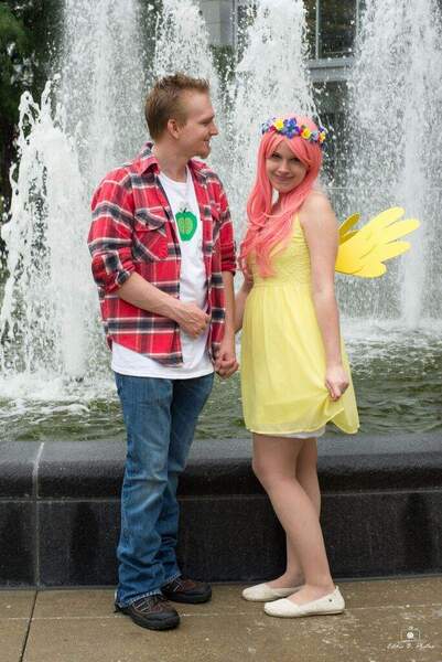 Size: 684x1024 | Tagged: safe, derpibooru import, big macintosh, fluttershy, human, 2015, clothes, cosplay, costume, cutie mark, cutie mark on clothes, denim, dress, duo, duo male and female, female, floral head wreath, flower, fluttermac, fountain, holding hands, image, irl, jeans, jpeg, looking at you, male, pants, photo, plaid shirt, shipping, shirt, shoes, smiling, smiling at you, straight, t-shirt, wig, wings