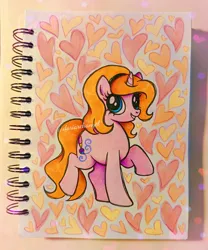 Size: 2320x2784 | Tagged: safe, artist:dariarchangel, derpibooru import, oc, oc:dazha, unofficial characters only, pony, unicorn, g4, big eyes, blue eyes, chubby, cute, female, headband, heart, horn, image, looking up, mare, ocbetes, orange hair, orange mane, orange tail, photo, pink coat, png, raised hoof, sketchbook, small horn, smiling, solo, standing, standing on two hooves, tail, traditional art