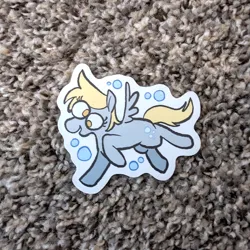 Size: 971x971 | Tagged: safe, artist:punkittdev, derpibooru import, derpy hooves, pegasus, pony, g4, blonde mane, blonde tail, bubble, carpet, colored, derp, eye clipping through hair, eyelashes, female, flat colors, gray coat, image, irl, mare, no catchlights, no pupils, open mouth, open smile, photo, png, raised hoof, raised leg, running, small wings, smiling, solo, spread wings, sticker, sticker design, tail, wings