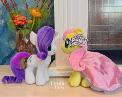 Size: 4284x3427 | Tagged: safe, derpibooru import, official, fluttershy, rarity, pegasus, pony, unicorn, g4, cape, clothes, double dove, dress, duo, duo female, female, flower, horn, image, indoors, irl, jpeg, looking at each other, looking at someone, merchandise, outfit, photo, plushie, pony plushie, reesee, smiling, symbiote studios, text, vase